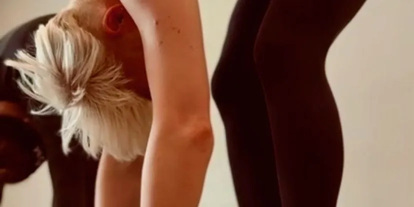 Close view of a student with short bleached hair folding forward, arms hanging, beside someone in dark leggings