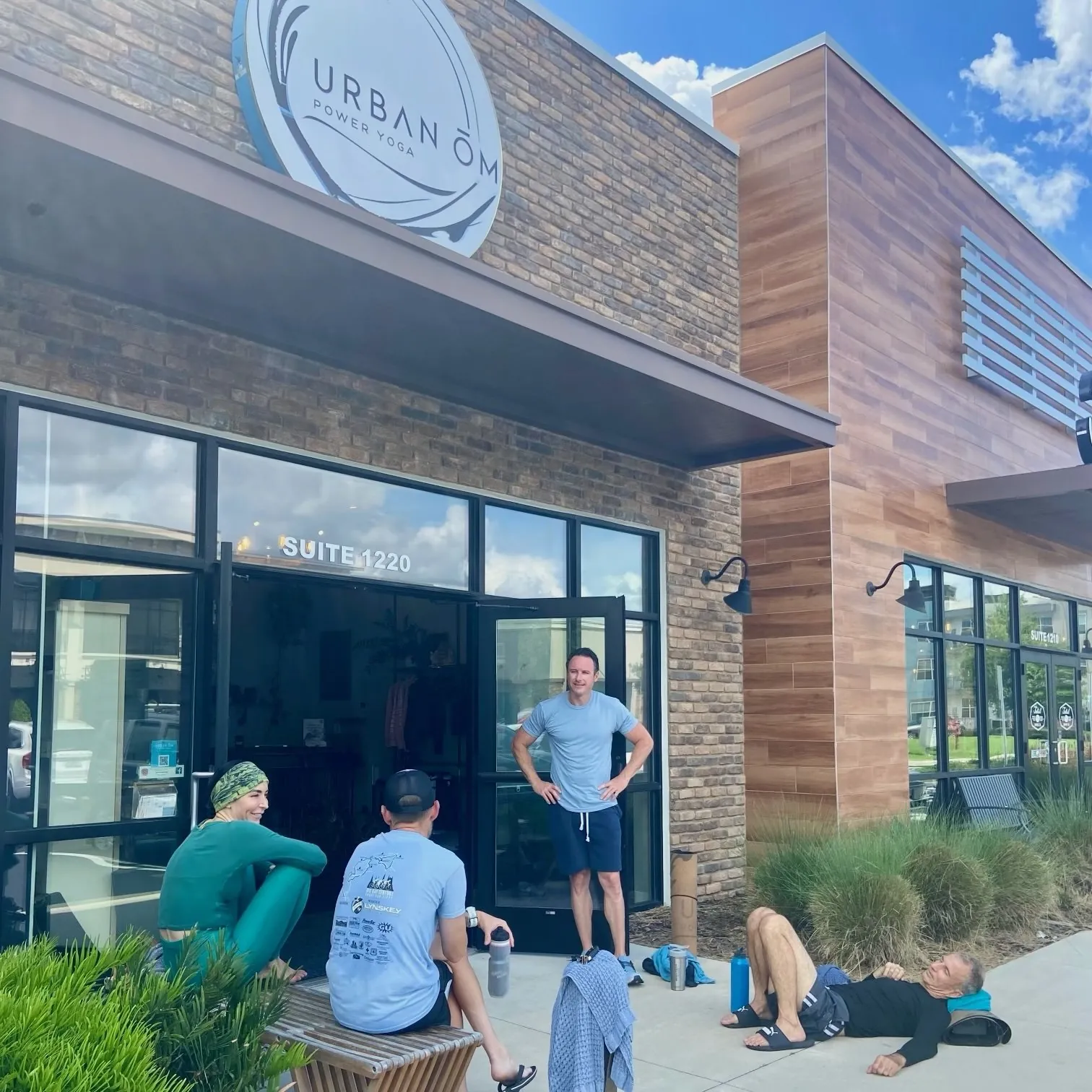 Urban Ōm Power Yoga storefront in Heathrow, with the round studio sign over the brick facade and students outside the Suite 1220 door